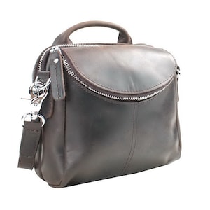 May include: A dark brown leather crossbody bag with a top handle and a silver zipper. The bag has a curved flap and a detachable shoulder strap with silver hardware. The bag is approximately 10 inches wide and 8 inches tall.