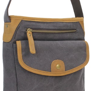 May include: A gray canvas crossbody bag with a brown leather flap and trim. The bag has a zippered pocket on the front and a small pocket with a button closure.