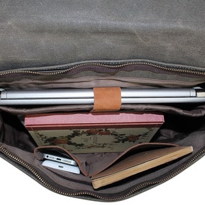 May include: A brown canvas messenger bag with a zippered top, open to reveal a laptop, a book, and a notebook. The bag has a brown leather strap and a brown leather handle.