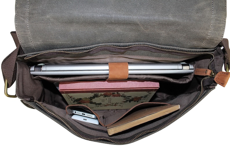 May include: A brown canvas messenger bag with a zippered top, open to reveal a laptop, a book, and a notebook. The bag has a brown leather strap and a brown leather handle.