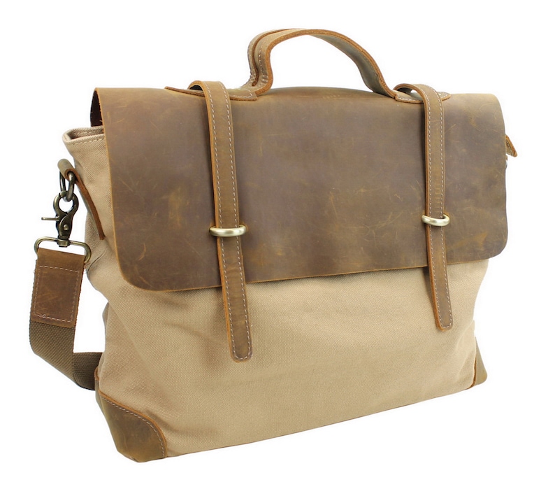 May include: A brown leather and beige canvas messenger bag with a top handle and adjustable shoulder strap. The bag has two leather straps with metal buckles.