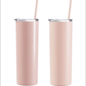 May include: Two pink insulated tumblers with clear lids and matching straws. The tumblers have a slender, cylindrical shape and a subtle glittery finish. The straws are inserted through the lids, ready for use. The background is plain white.
