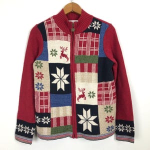 May include: A red zip-up cardigan with a patchwork design featuring snowflakes, reindeer, and plaid patterns. The cardigan has a ribbed collar and cuffs with a snowflake design. The zipper has a decorative charm.