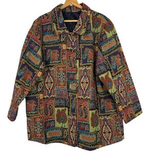 Puede incluir: Una chaqueta de manga larga con botones que presenta un patrón de tapiz multicolor con motivos repetidos de elefantes, pájaros y formas geométricas en tonos verde, rojo, azul y dorado. La prenda tiene un cuello estructurado y forro oscuro.