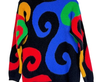May include: A black sweater with a crew neck featuring a vibrant, abstract design. The design includes large, swirling shapes in red, blue, green, and yellow. The sweater is hanging on a wooden hanger.