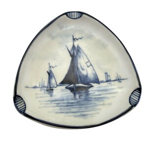 May include: Triangular ceramic ashtray with a nautical theme. The ashtray features a hand-painted scene of sailboats on the water in shades of blue and white. The rim is outlined in dark blue with decorative accents.
