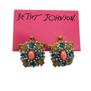 Puede incluir: Un par de pendientes Betsey Johnson en tono dorado con un diseño de tortuga con pedrería azul, verde, rosa y blanca.