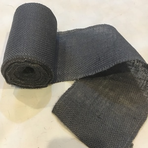 May include: A roll of dark gray burlap ribbon. The ribbon is woven and has a rough texture.