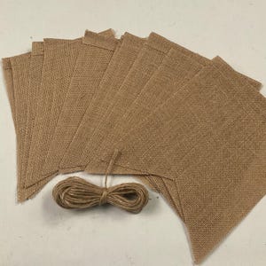 May include: A set of brown burlap pennant flags with a roll of twine for hanging. The flags are made of a natural, rustic material and are perfect for adding a touch of farmhouse charm to any event.