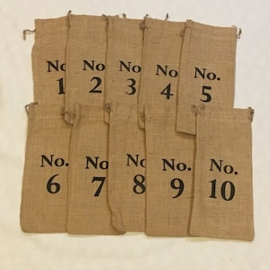 以下が含まれることがあります： 1から10までの黒い数字が印刷された、茶色のジュート製の袋が10個。袋は一列に並んでいます。