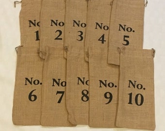 May include: Ten brown burlap bags with black numbers from 1 to 10 printed on them. The bags are lined up in a row.