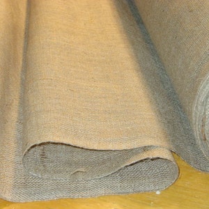 May include: Two rolls of natural brown burlap fabric, folded and stacked on top of each other. The fabric has a rough, textured surface.