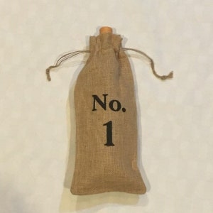 以下が含まれることがあります： 木製のトップと前面に「No. 1」の文字が印刷された、茶色のジュート製のワインボトルバッグです。