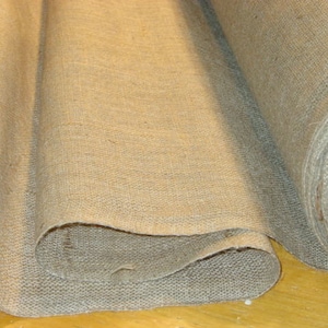 May include: Two rolls of natural brown burlap fabric, folded and stacked on top of each other. The fabric has a rough, textured surface.