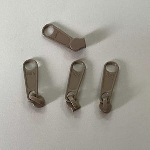 May include: Four brown zipper pulls with the text "YKK" printed on each.