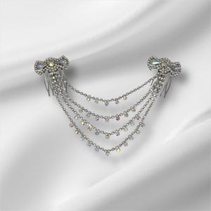May include: A silver-toned hair accessory featuring two decorative combs connected by four draped chains. Each comb is adorned with clear rhinestones and iridescent crystals. The chains are also embellished with small, sparkling clear stones.