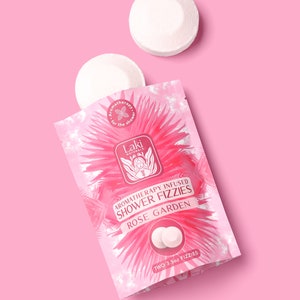 May include: A pink pouch with a white label that says "Aromatherapy Infused Shower Fizzies Rose Garden" and "Two 3.5oz Fizzies". There are two white shower fizzies in the pouch.