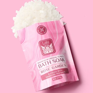 May include: A white pouch with pink marbling containing white magnesium crystal flakes. The pouch has a red label that reads "Laki Naturals Magnesium Crystal Flakes Bath Soak Rose Garden Blended with Hawaiian Sea Salts 8oz-277g".