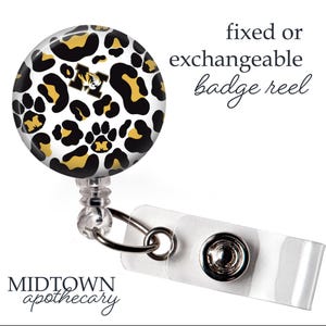 May include: A badge reel with a round, leopard print design in black, gold, and white. The reel has a clear plastic strap and a metal clip. The text "fixed or exchangeable badge reel" is visible.