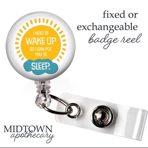 May include: A white badge reel with a round design featuring the text "I NEED TO WAKE UP SO I CAN PUT YOU TO SLEEP." The design includes a yellow sun and a blue cloud. The reel is attached to a clear plastic strap.