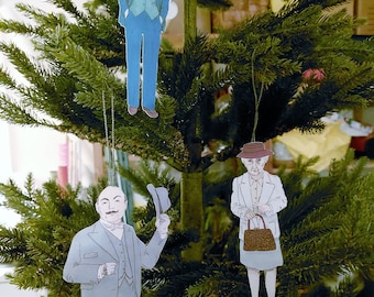 May include: Three paper ornaments hanging on a Christmas tree. The ornaments are cutouts of people wearing suits and hats. One ornament has the text "Good Luck" on it.