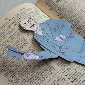 May include: A blue paper cutout of a man wearing a suit and a hat. The man is holding a book open to a page with the word "limosis" highlighted. The book is titled "lineup".