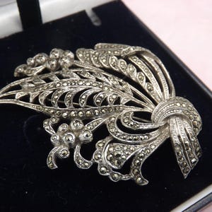 A beautiful large flower spray vintage jewelry brooch made in polished openwork silvertone set with sparkly faceted marcasites stones