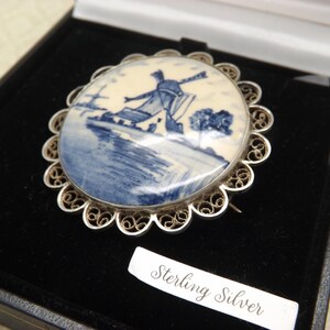 Pode incluir: Um broche de filigrana de prata com um camafeu de porcelana azul e branco que representa um moinho de vento. O camafeu est&aacute; engastado em uma moldura de filigrana de prata e o broche &eacute; marcado com "Sterling Silver".