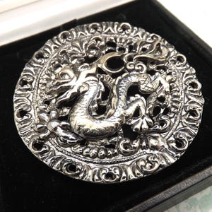 May include: A white ceramic mug with a black handle and the text "But First, Coffee" in a black, bold font. The mug is on a white surface. The mug is approximately 4 inches tall.