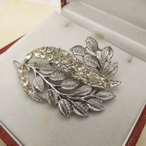 Een fijne vintage vintage sieradenbroche met bloemen en bladeren van zilverkleurig metaal bezet met ronde, sprankelende, gefacetteerde helderwitte stenen