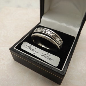 Pode incluir: Um anel de prata com um design de nó celta, em uma caixa de anel preta com um rótulo "Sterling Silver".