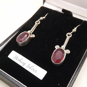 May include: A pair of sterling silver earrings with red gemstone drops. The earrings are in a black jewelry box with a label that reads "Sterling Silver".
