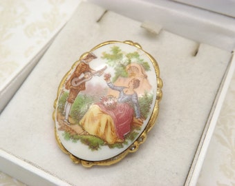 Une jolie broche de bijoux vintage ovale en porcelaine Fragonard en métal doré avec une plaque en porcelaine peinte d'un couple dans un jardin