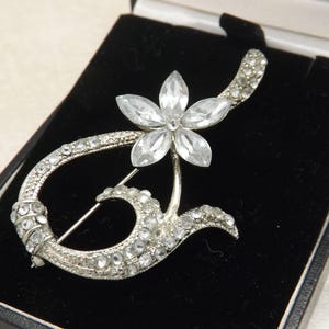 Een mooie vintage vintage sieradenbroche met abstracte bloemen en bladeren van zilverkleurig metaal bezet met ronde, sprankelende, gefacetteerde helderwitte stenen