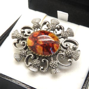 A fine Scottish Celtic oval thistle vintage jewelry brooch made in antiqued silvertone metal and set with a shiny mixed striped brown stone