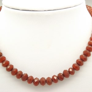 May include: A necklace made of faceted carnelian beads. The beads are a deep orange-red color and are strung on a clear cord. The necklace is approximately 18 inches long.