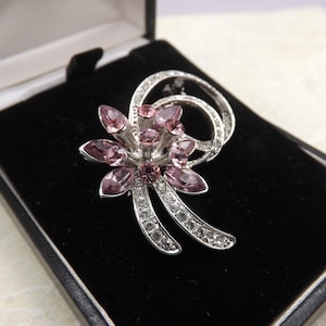 Une belle broche de bijoux vintage en forme de gerbe de fleurs abstraites en métal argenté, sertie de pierres roses scintillantes et blanches transparentes