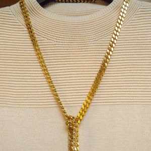 Un hermoso collar de cadena de bisutería de estilo de eslabones planos largos con barras cruzadas hecho en un metal chapado en oro brillante, pulido y calado.