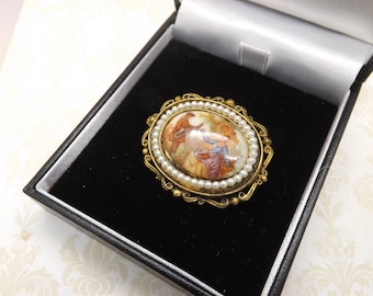 Um fino broche oval estilo Fragonard com pérolas de metal dourado e uma placa de porcelana pintada com um casal em um jardim