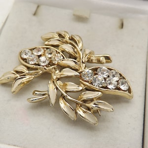 A lovely classic flower and leaf design vintage jewelry brooch in goldtone openwork metal and enamel with sparkly clear white stones