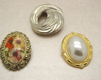 A lovely group of three goldtone and silvertone mixed design vintage jewelry scarf clips in various colours, shapes, finishes and sizes