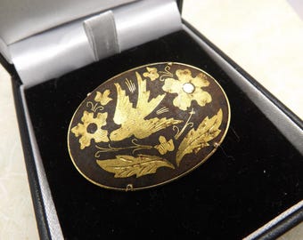 Um lindo broche oval vintage de Damasco decorado com um desenho gravado de um pássaro e flores, feito em metal dourado e esmalte preto.