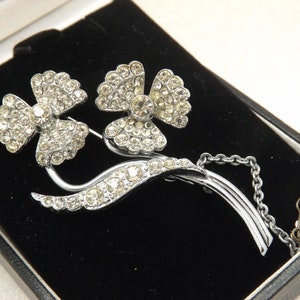 Een mooie vintage vintage sieradenbroche met abstracte bloemen en bladeren van zilverkleurig metaal bezet met ronde, sprankelende, gefacetteerde helderwitte stenen