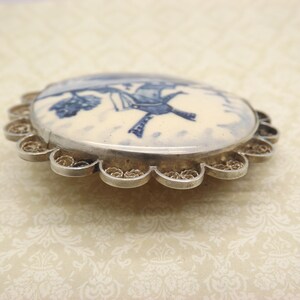 Pode incluir: Um broche de filigrana de prata com um camafeu de porcelana branca com um design de moinho de vento azul e branco.