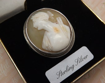 A beautiful Victorian hand carved cameo antique jewelry brooch made with a silver mount set with a shell cameo of a young maiden