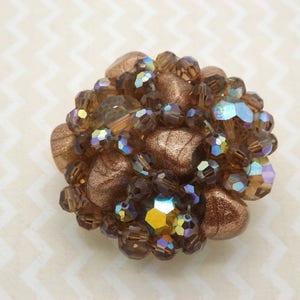 May include: A cluster of iridescent brown glass beads and stones, arranged in a circular shape, creating a decorative brooch.
