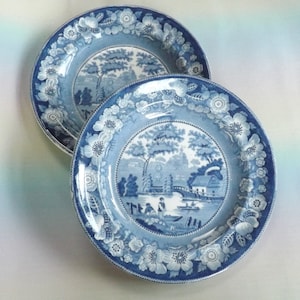 Może przedstawiać: Dwa niebiesko-białe talerze porcelanowe z kwiatowym obramowaniem i sceną chatki nad rzeką z mostem.