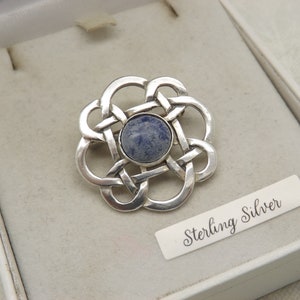 A lovely round polished solid silver vintage period brooch made in a raised open work design in 925 silver and set with a smooth blue stone