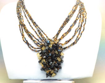 A fine hand made multi strand center drop necklace made up of rows of shiny polished mixed shape colour and size glass and gemstone beads