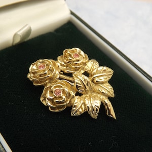 A superb triple rose flower spray design vintage jewelry brooch made in raised work goldtone metal with each rose set with a pink stone
